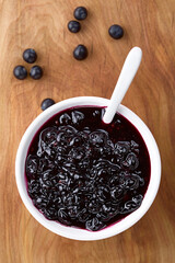 Fresh homemade jam made of Patagonian Calafate berries (lat. Berberis heterophylla) served in white bowl with spoon, photographed overhead on wood (Selective Focus, Focus on the jam)