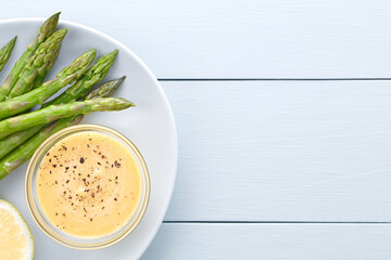Fresh cooked green asparagus with Hollandaise sauce and lemon served on blue plate, photographed overhead with copy space on the side (Selective Focus, Focus on the top asparagus stalks and the sauce)