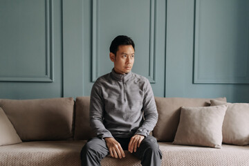 Asian man in fleece sitting in the living room in cold weather.