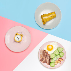 Plates with food, alarm clock and measuring tape top view on pink, blue and white background.