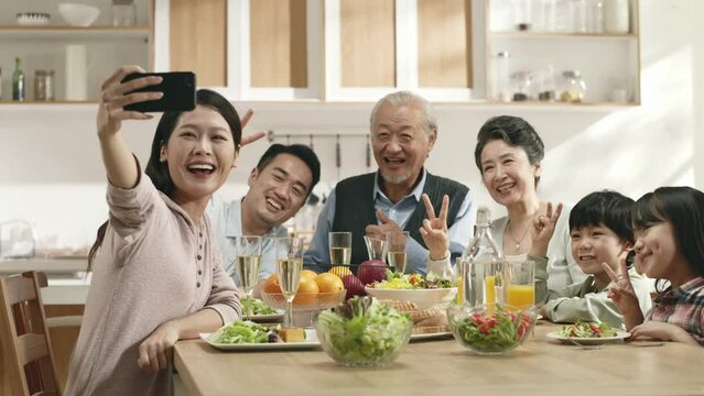 happy three generation asian family sitting at dining table taking a selfie at home