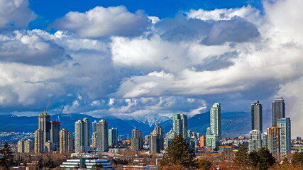 New residential area of  high-rise buildings in the city of Burnaby, construction site in the center of the city against the backdrop of snow covered mountain range and blue cloudy sky