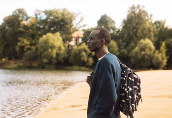A young black man in sportswear with a backpack walks near the lake.