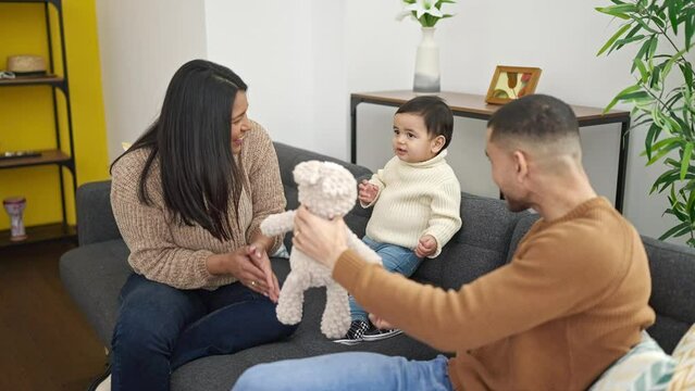 Couple and son playing with teddy bear sitting on sofa at home