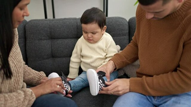 Couple and son sitting on sofa putting shoes to baby at home