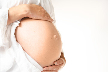 Cropped shot of unrecognizable pregnant woman touching belly standing by white wall.Copy space,...