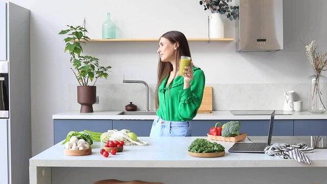 An attractive woman drinks a green smoothie in the kitchen. Healthy eating