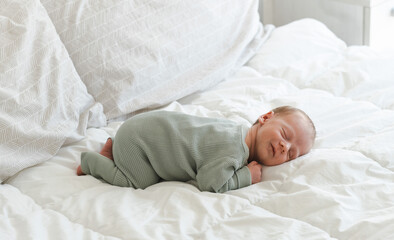 Cute caucasian several days old newborn smiling while sleeping on white blanket at home.Adorable,calm, innocent baby indoors.Copy space. Full body shot.Minimalism,lifestyle.