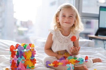 Happy cute caucasian two years old toddler, girl playing with colourful toy circles on bed at home...