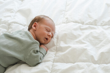 Cute caucasian several days old newborn sleeping with open mouth on white blanket at home.Adorable,calm, innocent baby indoors.Copy space. Half body shot.Minimalism,lifestyle.  - obrazy, fototapety, plakaty
