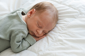 Cute caucasian several days old newborn sleeping on stomach on white blanket at home.Adorable,calm,...
