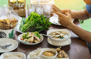 Spicy Vietnamese Pork Sausage Salad (Yum Moo Yor). Pork sausage spicy salad Thai and Vietnam food with other appetizing dishes and vegetables on wooden table with young man using mobile phone.