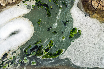 Top view of wastewater with air bubbles and moss flowing through a cracked ditch. Oxygen bubble in...