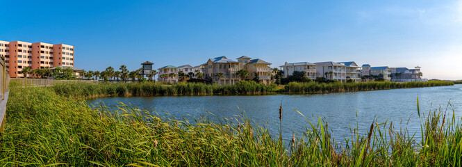 Obraz premium Destin, Florida- Panorama of lagoon with tall grass on the shore in a residential area. There is an apartment building on the left and three-storey homes on the right near the lagoon.