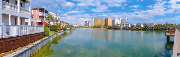 Fototapeta na wymiar Destin, Florida- Panorama of a community with lake with brackish water. Lake with steel seawall surrounded by single-family homes and multi-storey residences.