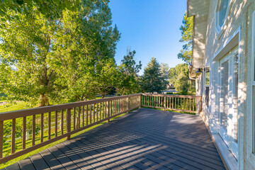 Views of trees and lawn with white fence from the terrace with wooden flooring and railings. There is a double door near the windows on the left of the terrace and views of the yard on the right.