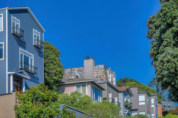 Fototapeta na wymiar Multi storey houses on a sunny day in San Francisco California residential area.. Facade of homes on a bright neighborhood viewed from the street against blue sky background.