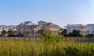 Fototapeta na wymiar Lavish multi storey houses in Destin Florida with terraces overlooking a lagoon. Tall green grasses and expansive blue sky can also be seen in this scenic landscape on a sunny day.