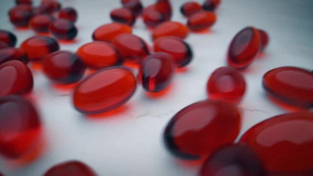 Red krill oil capsules bouncing over a white table. Slow motion.