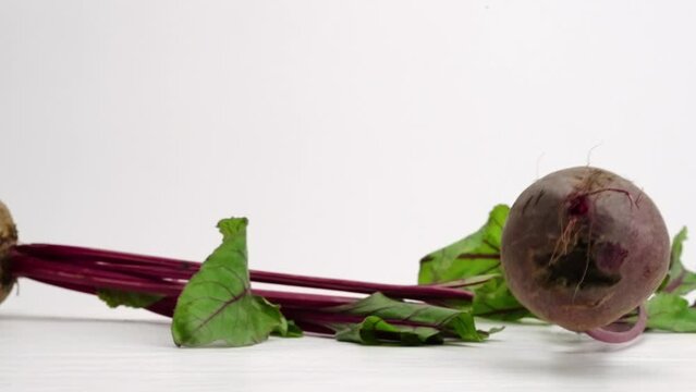 Whole beet roots falling and bouncing on white studio backdrop in 4k slow motion
