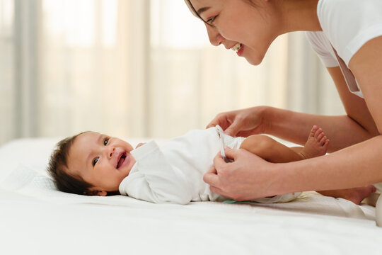 mother changing diaper of newborn baby while lying on bed