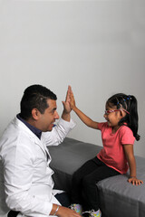 Pediatrician doctor and 4 year old latin girl patient in consultation are friends and make hi five sign and bump fists
