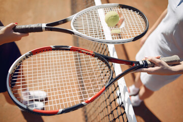 Cropped photo of two rackets and ball in hands of female tennis players