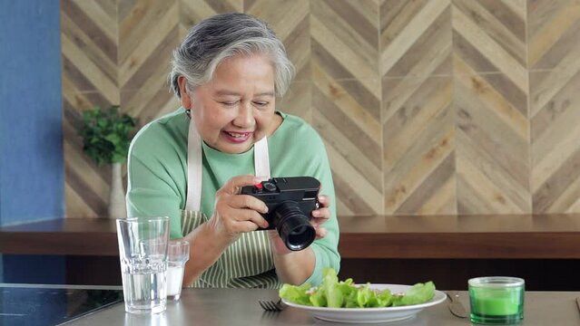 Healthy elderly Asian woman taking pictures of food in the kitchen at home. The concept of modern seniors living in retirement to be happy.