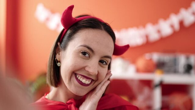 Young beautiful hispanic woman wearing devil costume make selfie by camera at home