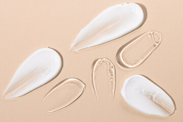 Swatch of white cosmetic cream, liquid transparent gel on beige background, flat lay. Samples of...