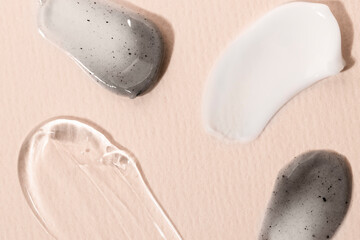 Samples of cream, liquid peptide, charcoal face mask, body scrub on a beige background, flat lay. Care products, cosmetic texture macro, top view.