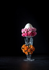 Easter egg in a glass vase with roses on a black background