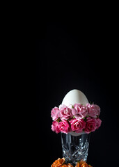 Easter egg in glass vase with pink flowers on black background