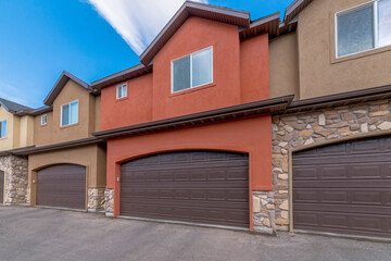 Townhouses with attached garages and painted orange and brown stucco and stone veneer walls. There...