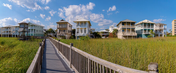 Wooden pathway with railings heading to the homes on the beach at Destin Point, Destin, Florida. Panorama of a residential area with tall grasses below the footbridge at the front of houses.