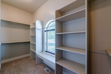 Carpeted empty walk-in closet with floor vent and arched window. There is a window on the left with...