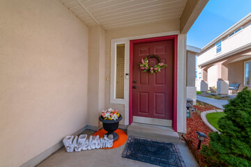 Wine red front door with wreath and sidelight near the beige stucco wall. Entrance of a house with...