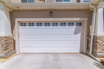 Garage exterior with white garage door with window panels. There are two columns with rain drainage pipe on the right side of the garage door under the wall light above.