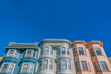 Charming homes with bay windows and colorful walls against vibrant blue sky. Exterior view of multi-storey houses with cloudless sky background in San Francisco California.