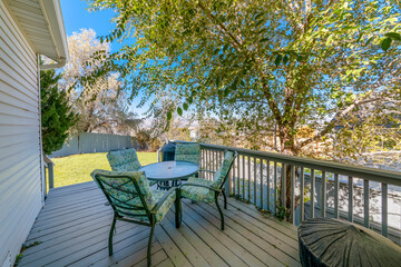 Obraz premium House deck with dining table with cushioned seats near the railings beside the tree. Deck of a house with views of the backyard with lawn and fence panel wall.