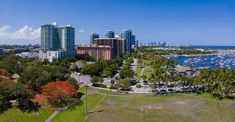 Aerial view of a park near modern city buildings near the harbor at Miami, Florida. There is a park at the front with grass field near the harbor on the right at the front of multi-storey buildings.