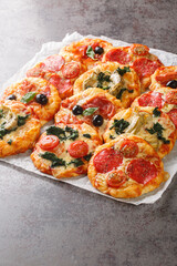 Mix mini pizza or Pizzette with various toppings close-up on parchment on the table. Vertical