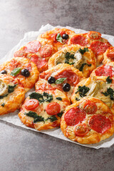 Homemade Mini Pizzas Pizzette with meaty and vegetarian toppings close-up on parchment on the table. Vertical