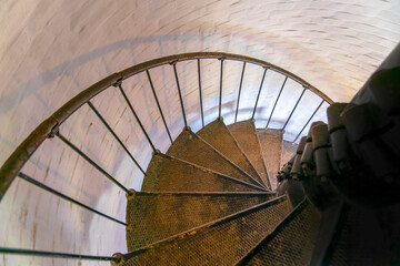 Fototapeta premium Spiral stairs inside Cape Florida Lighthouse in Bill Baggs Cape Florida State Park- Miami, Florida. Perspective view of a rusty spiral stairs heading downstairs beside the painted white bricks wall.