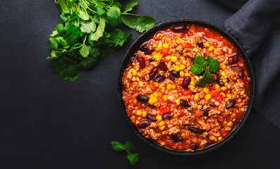 Chili con carne with beef, red beans, paprika, corn and hot peppers in tomato sauce, spicy tex-mex dish in a cooking pot, black table background, top view