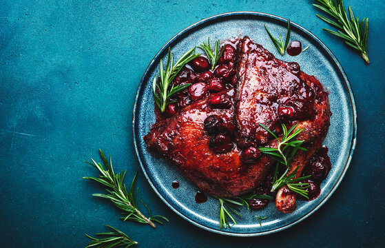 Baked duck legs in cherry and red wine sauce with rosemary. Delicacy dinner. Blue table background, top view