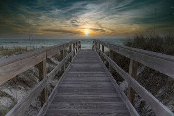 Fototapeta na wymiar Straight wooden pathway with railings in between sand dunes against the ocean and horizon sky. Wooden walkway near the protected sand dune with grasses with views of ocean waves in Destin, Florida.