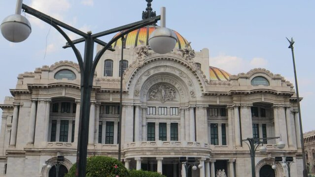 A full shot with tracking of the Palacio de Bellas Artes in Mexico City, with street lamps in the foreground, on a clear day with blue sky.