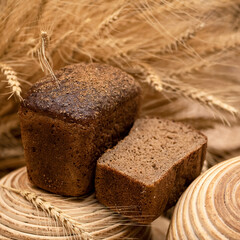 Homemade dark rye sourdough bread with coriander. Healthy diet. Loaf of bread in shape of brickin cut form on wooden stand among spikelets of wheat. Grain harvest. Soft focus, side view. 