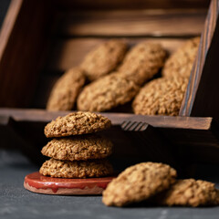 Homemade oatmeal cookies. Three cookies are stacked. Wooden display case with cookies in background. Healthy sweets. Dark background. Side view. Soft focus.